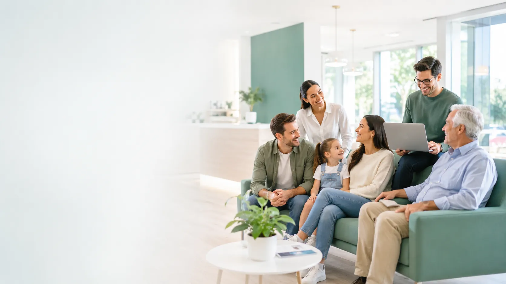 Adults, a child, and an older adult gathered around a laptop in a bright living room.