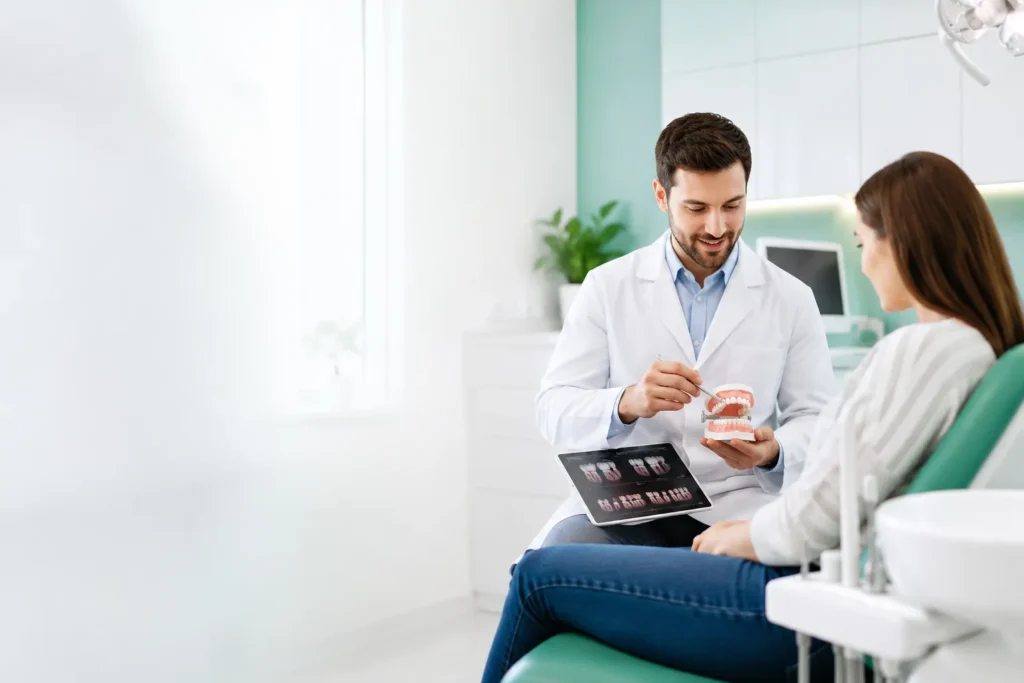 Dentist explaining dental treatment options to a patient using dental models in a bright modern office.