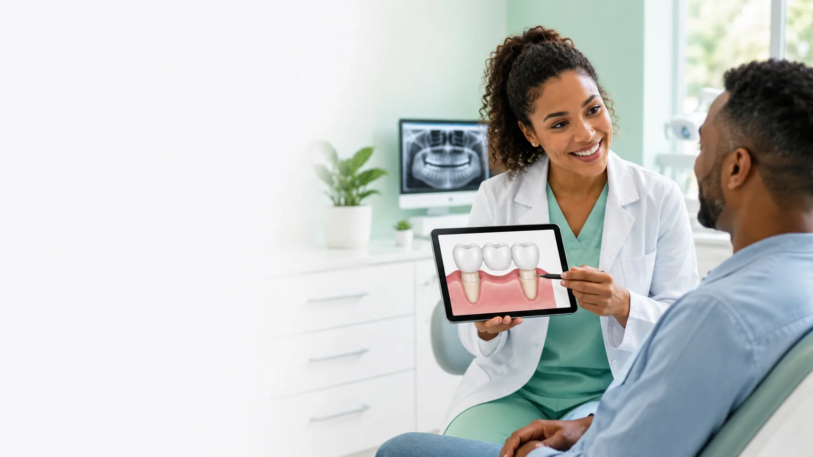 Dentist explaining a dental bridge to a patient using a tablet in a modern dental office.